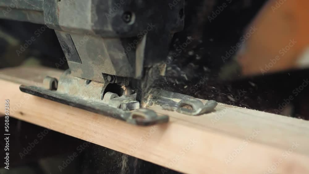 Close-up, a carpenter in his workshop saws an electric jigsaw, a wooden board, makes furniture parts. Woodwork.Slow-motion Carpenter saws wood, processing it. Home Repair Construction Tools Close-up, a carpenter in his workshop saws an electric jigsaw, a wooden board, makes furniture parts. Woodwork.Slow-motion Carpenter saws wood, processing it. Home Repair Construction Tools