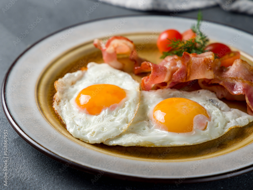 Fried eggs with tomatoes and bacon on blue concrete table macro close up Fried eggs with tomatoes and bacon on blue concrete table macro close up
