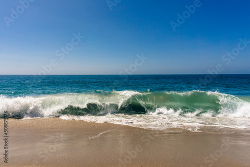 Seascape of turquoise wave crushing onto sandy beach on a warm sunny day