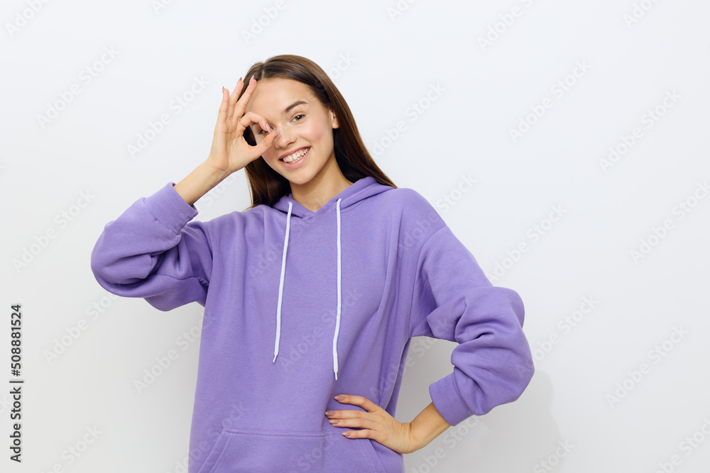 a sweet attractive woman standing on a white background in a purple tracksuit, smiling broadly, leaned her hand against her eye in the form of an OK sign, putting her other hand on her waist a sweet attractive woman standing on a white background in a purple tracksuit, smiling broadly, leaned her hand against her eye in the form of an OK sign, putting her other hand on her waist