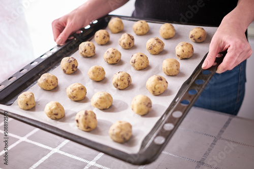 Woman holding baking tray full of raw dough ball while making Chocolate chip cookies