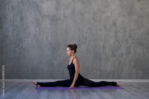 Caucasian young cool attractive yoga woman practicing yoga concept, standing in exercise in workout pose, wearing sports bra and pants, full length against gray wall