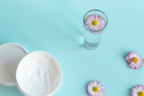 Fresh flowers, daisies are laid out in a corner, with a glass of clean water and a white jar with a cream cosmetic on a blue background and a free space for advertising.