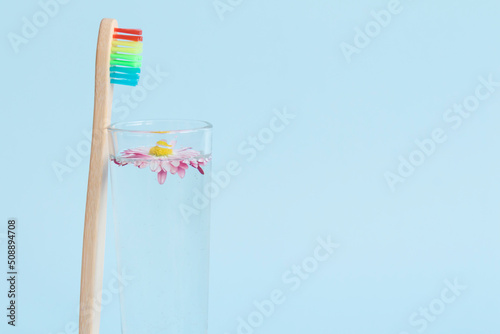 An ecological wooden toothbrush, a glass with clean, clear water and a white daisy on a blue background. And an empty space for advertising dentistry.