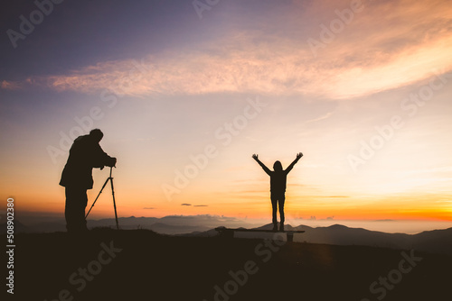 Fototapeta Silhouette of photographer taking photo with model on mountain at sunset, profes