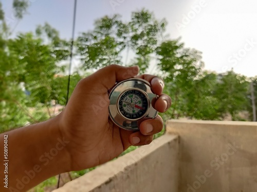 Picture of a compass made of metal shot against blur background in summers during daylight used for directions by travelers
