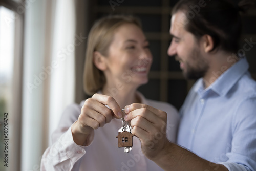 Relocation day, cohabitation, new house for young family, bank loan, happy clients of new first real-estate purchase concept. Blurred married 30s couple holding keys showing to camera close up view