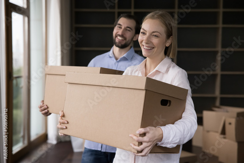 Young wife and husband holding boxes with personal belongings pose in unfurnished living room. Happy homeowner family portrait, moving day, start new life at own or rented dwelling, repairs concept © fizkes