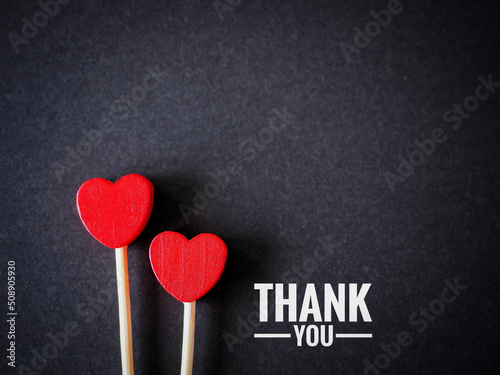 The words thank you message and two red heart on the black paper background. top viwe, flat lay with copy space. Greeting card.. photo