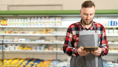 Photography Young bearded sales clerk using digital tablet and working at supermarket
