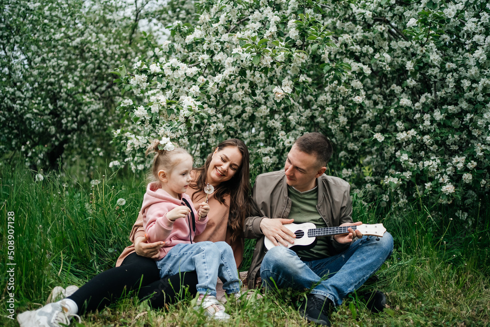  family mom mom baby daughter in the garden blooming apple trees, father playing the ukulele