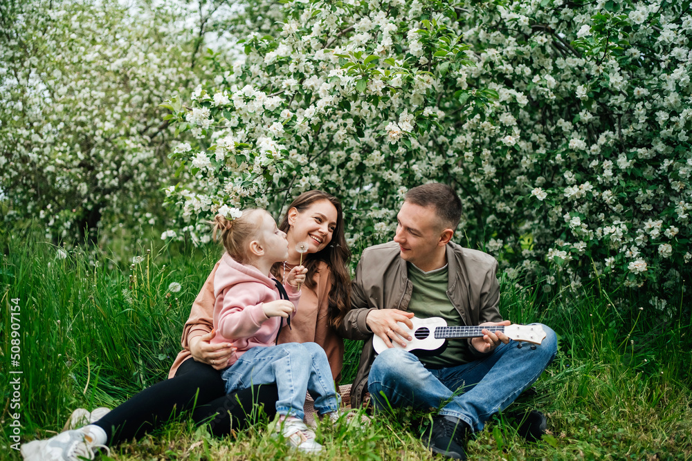 family mom mom baby daughter in the garden blooming apple trees, father playing the ukulele family mom mom baby daughter in the garden blooming apple trees, father playing the ukulele