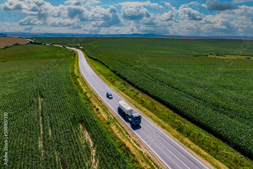 fuel delivery. blue truck driving on asphalt road along the green fields. seen from the air. Aerial view landscape. drone photography. cargo delivery. transportation concept