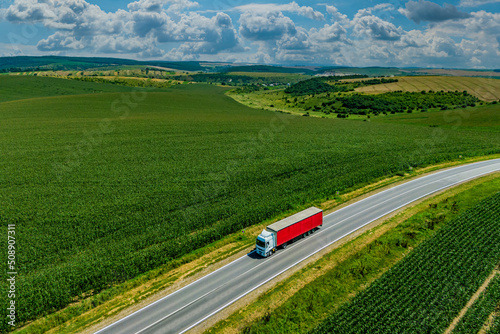 red truck driving on asphalt road along the green fields. seen from the air. Aerial view landscape. drone photography. cargo delivery and transportation concept