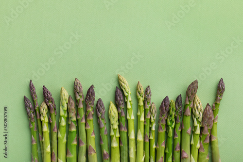 Heap of fresh asparagus on green background top view. Healthy food in flat lay style. photo