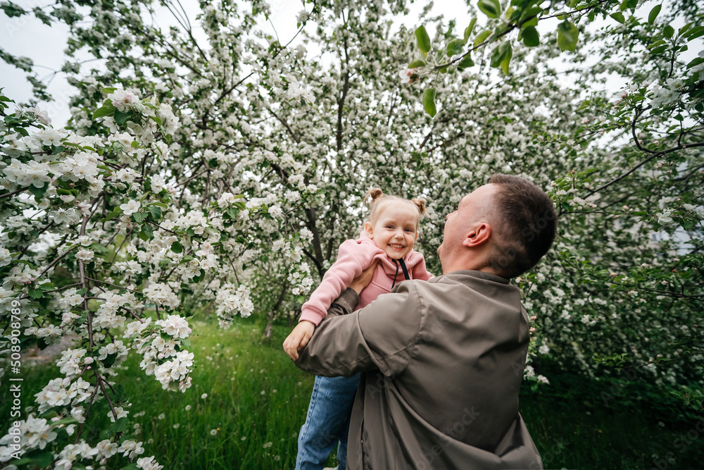 dad holds a joyful baby daughter in his arms in a garden with a blooming apple tree dad holds a joyful baby daughter in his arms in a garden with a blooming apple tree