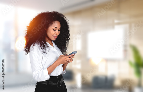 Fototapeta Black businesswoman with smartphone in hands, office room