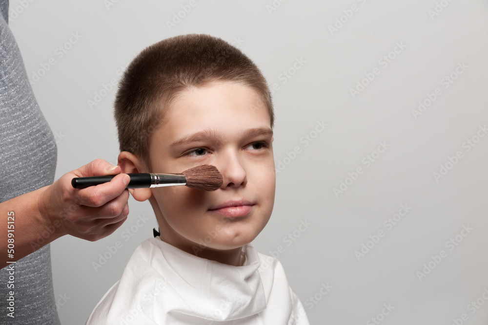 Applying makeup on the face of a caucasian boy. Cosmetic procedures on the face of a novice actor. Align skin tone Applying makeup on the face of a caucasian boy. Cosmetic procedures on the face of a novice actor. Align skin tone
