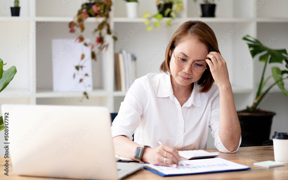 Asian aged-female senior college teacher in glasses reviewing and examining her college student's report in her modern house. Asian aged-female senior college teacher in glasses reviewing and examining her college student's report in her modern house.