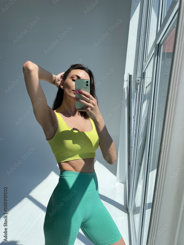 Fit tanned woman in sportswear, fitting blue leggings, perfect body, abs  motivation, take photo selfie on phone in mirror for social media, stories,  vertical. Stock Photo