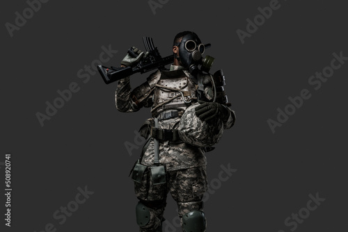 Studio shot of black military man holding rifle on his shoulder isolated on grey background.