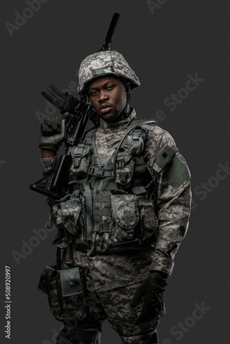 Photo of handsome military man of african ethnic armed with rifle isolated on gray.