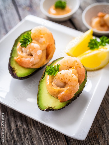 Avocado with fried prawns on and cocktail sauce on wooden background