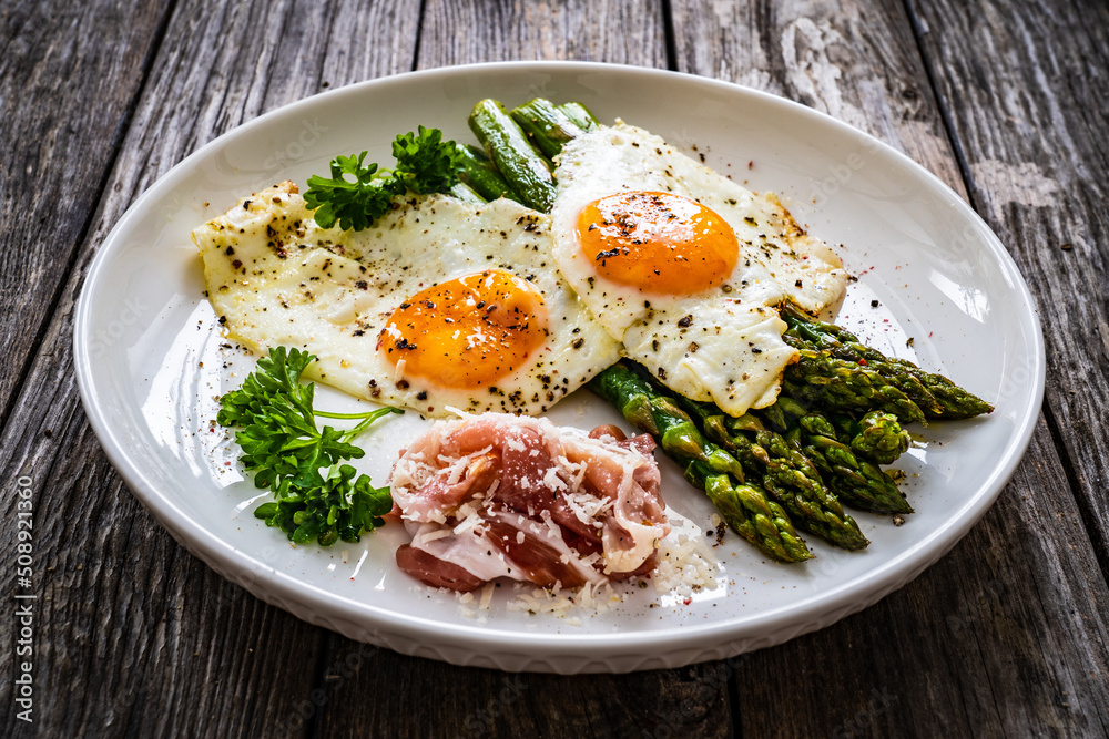 Sunny side up eggs with green asparagus fried bacon on black plate on wooden table
Sunny side up eggs with green asparagus fried bacon on black plate on wooden table