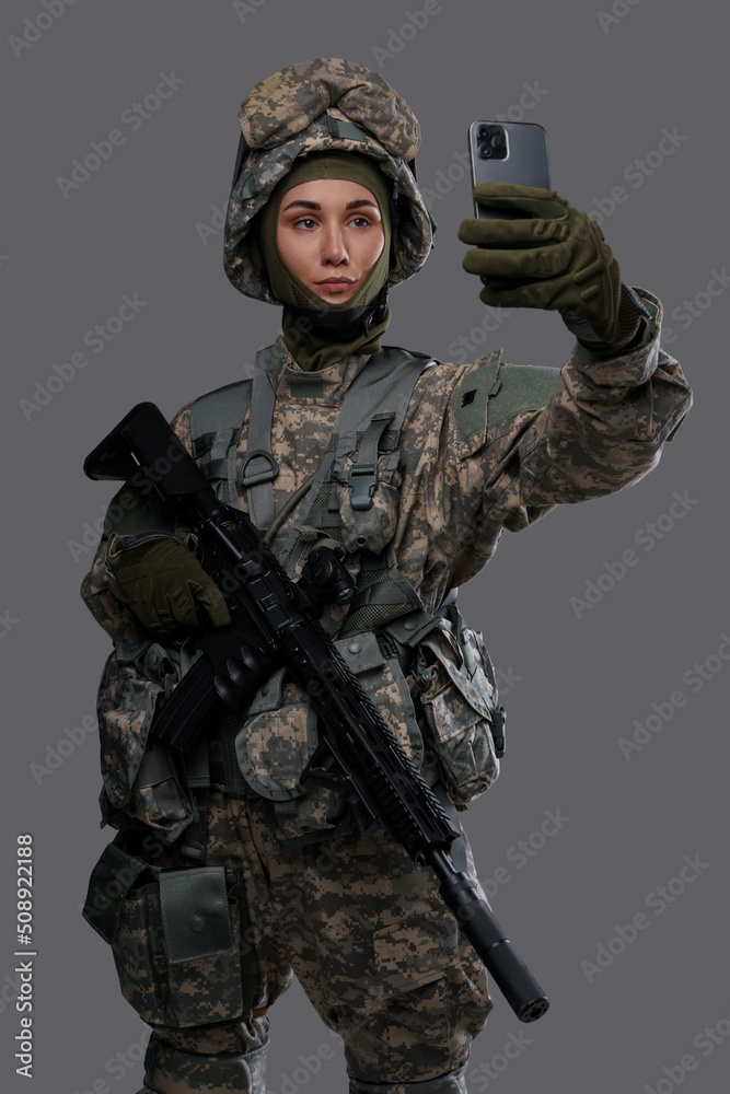 Shot of militant woman with smartphone and rifle isolated on gray background. Shot of militant woman with smartphone and rifle isolated on gray background.