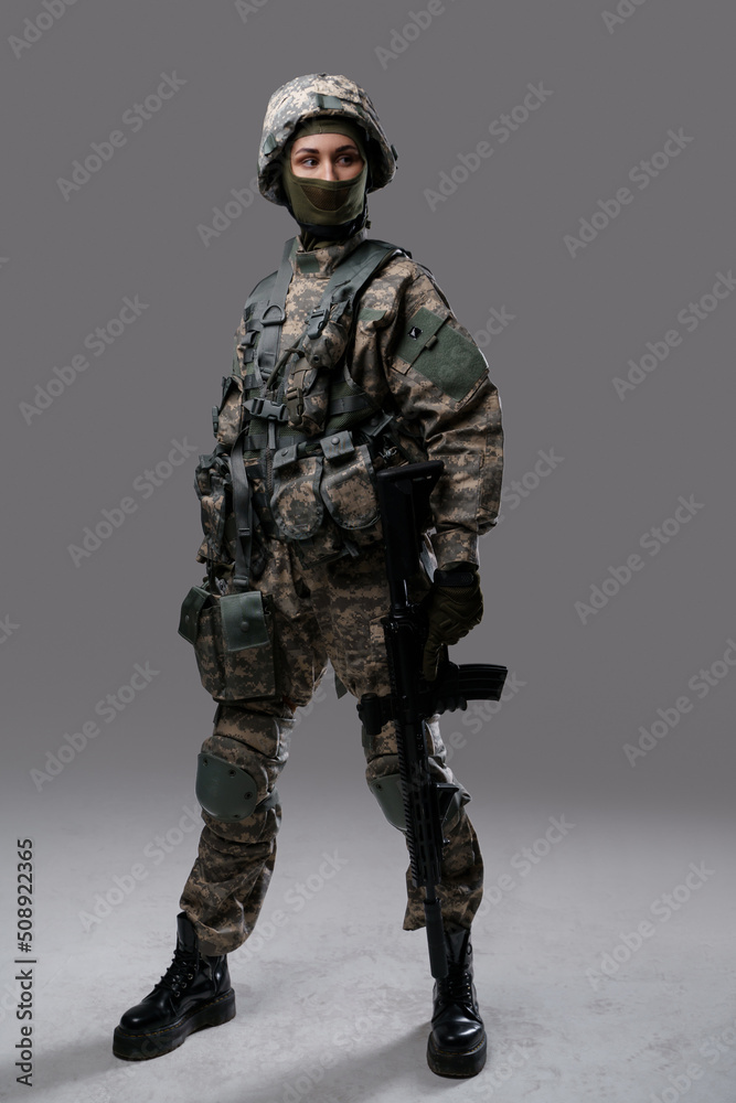 Photo of isolated on gray special forces woman holding rifle dressed in uniform with helmet. Photo of isolated on gray special forces woman holding rifle dressed in uniform with helmet.