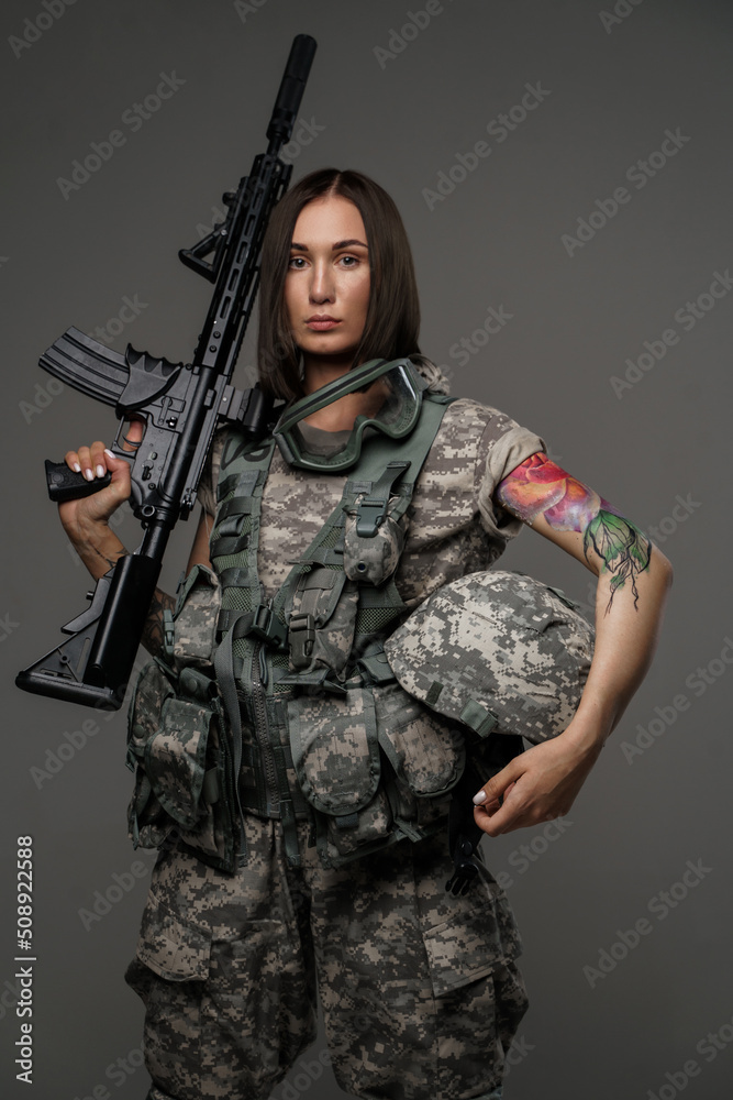 Photo of brown haired female soldier dressed in camouflage uniform holding rifle on her shoulder. Photo of brown haired female soldier dressed in camouflage uniform holding rifle on her shoulder.