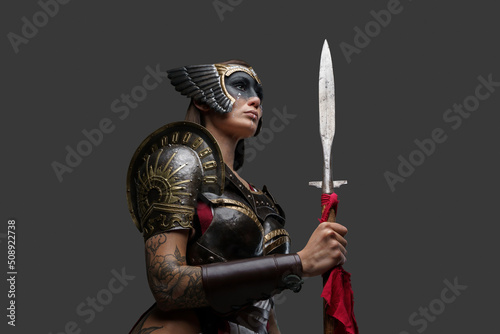 Studio shot of seductive woman barbarian dressed in armor and helmet holding spear. photo
