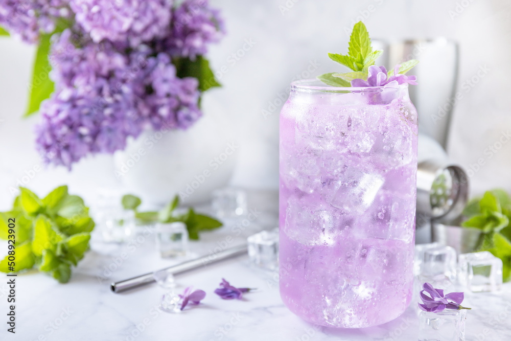 Lilac drink, infused drink from lilac flowers. Organic natural daikiri cocktail or mocktail, lilac lemonade with ice on a marble table. Lilac drink, infused drink from lilac flowers. Organic natural daikiri cocktail or mocktail, lilac lemonade with ice on a marble table.
