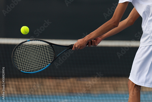 Male tennis player hitting backhand by net on the tennis court photo