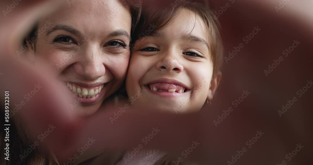 Close up portrait young woman and adorable little 6s daughter joining fingers making heart gesture look at camera feels overjoyed. Symbol of love, life value, cherish, happy motherhood, family concept Close up portrait young woman and adorable little 6s daughter joining fingers making heart gesture look at camera feels overjoyed. Symbol of love, life value, cherish, happy motherhood, family concept