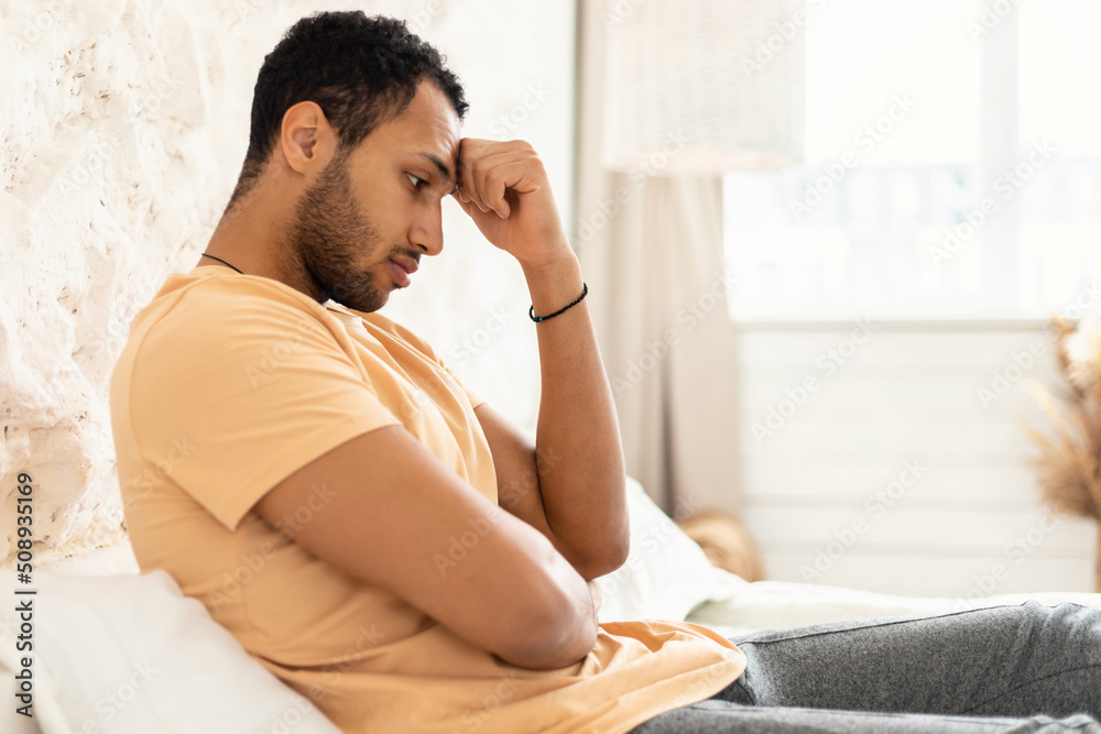 Side View Of Unhappy Depressed Arabic Man Sitting In Bedroom Side View Of Unhappy Depressed Arabic Man Sitting In Bedroom