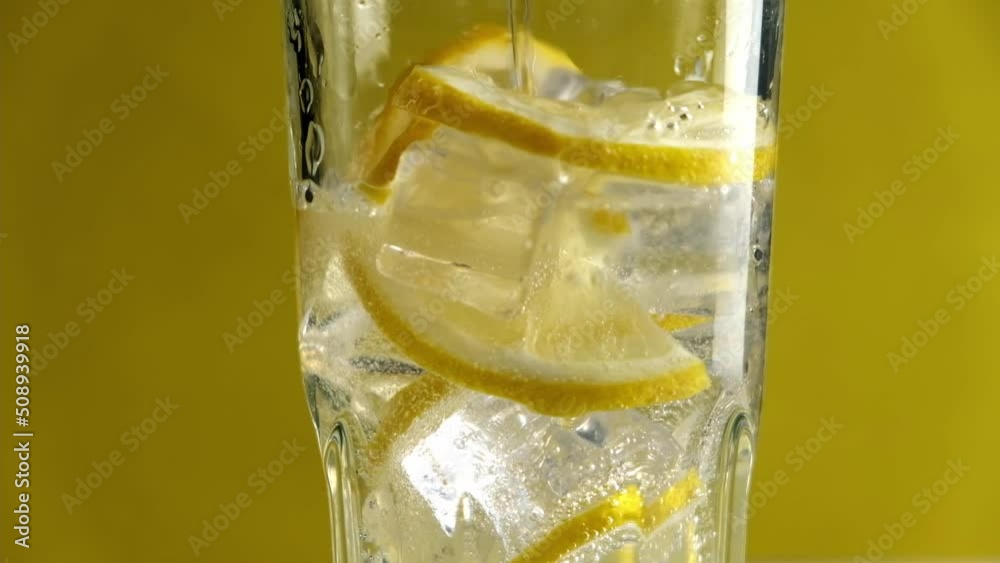 Close-up of a refreshing soda tonic. Pouring sparkling water into a glass with lemon and ice. Lemonade.