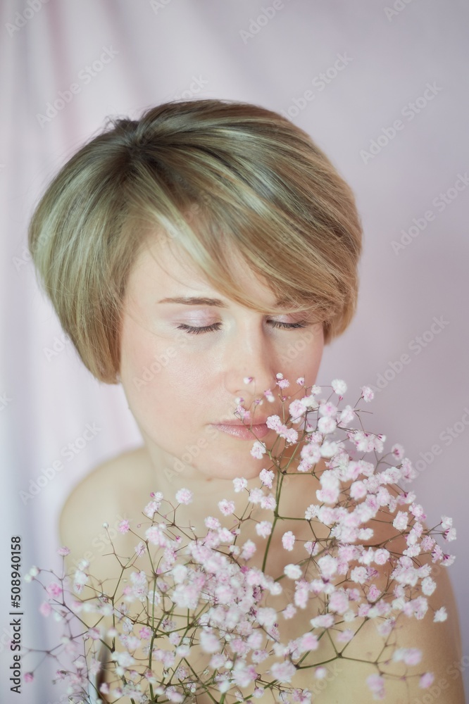 Naklejka premium Portrait of a girl on a pink background with flowers. Tenderness and feminine. The sphere of beauty and women's health. Short haircut, blonde hair