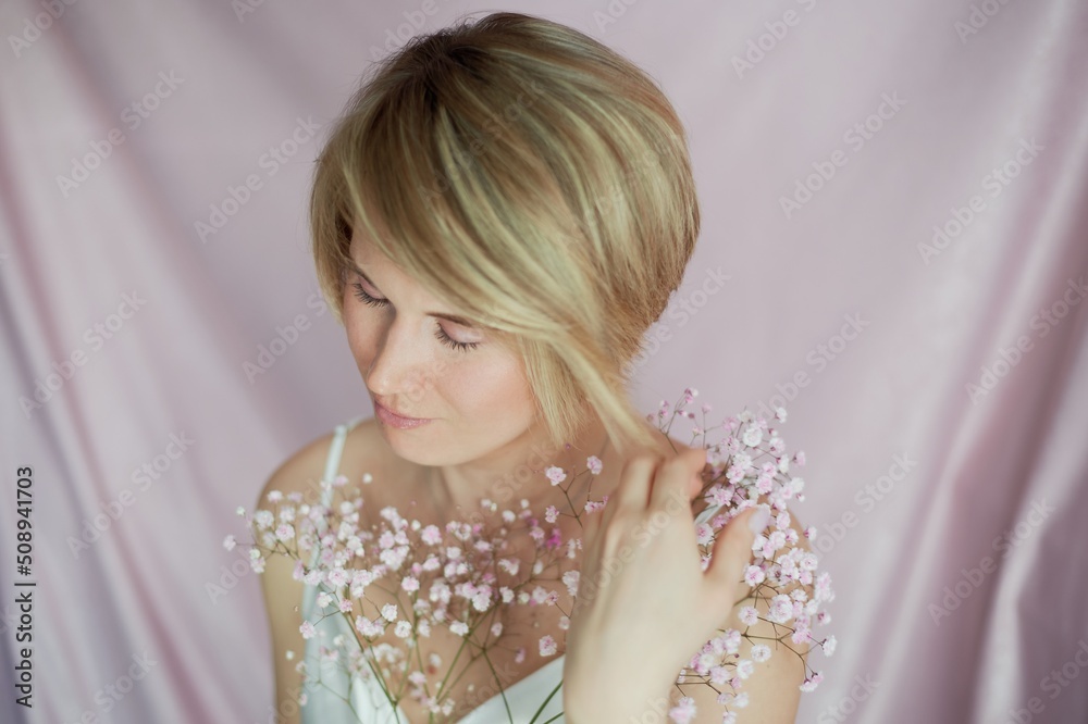 Portrait of a girl on a pink background with flowers. Tenderness and feminine. The sphere of beauty and women's health. Short haircut, blonde hair Portrait of a girl on a pink background with flowers. Tenderness and feminine. The sphere of beauty and women's health. Short haircut, blonde hair
