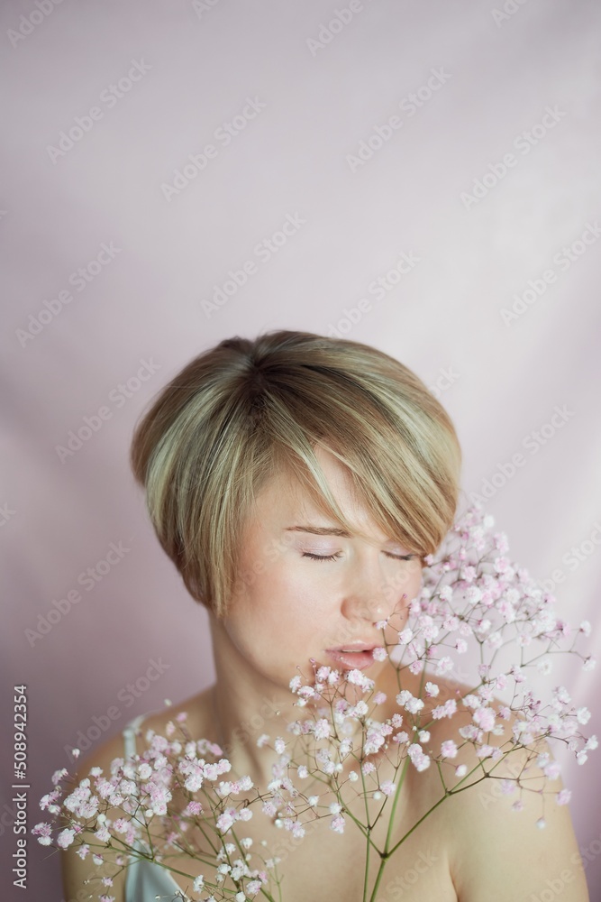Portrait of a girl on a pink background with flowers. Tenderness and feminine. The sphere of beauty and women's health. Short haircut, blonde hair Portrait of a girl on a pink background with flowers. Tenderness and feminine. The sphere of beauty and women's health. Short haircut, blonde hair