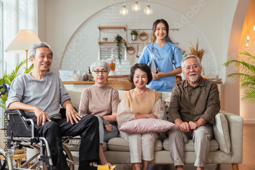 portrait of asian senior male female friend group sit of sofa smiling together in nursing home senior daycare with young nurse care giver in uniform look at camera group shot in living room cheerful