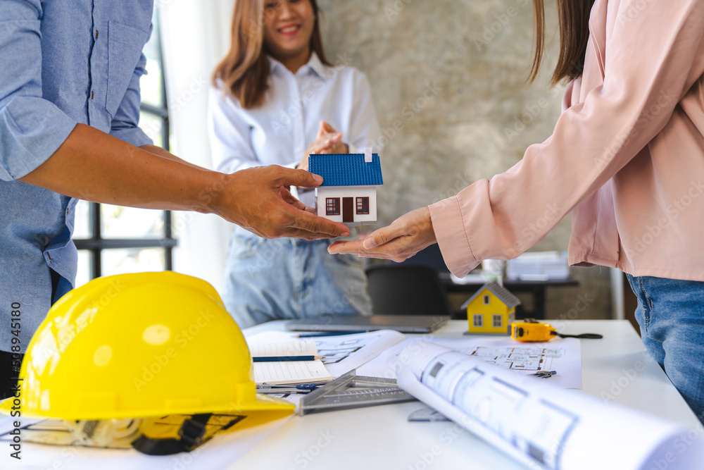 Construction and structure concept of Engineer or architect holding a model of house wood to present and give to the customer, the contract between the two companies' real estate concept Construction and structure concept of Engineer or architect holding a model of house wood to present and give to the customer, the contract between the two companies' real estate concept