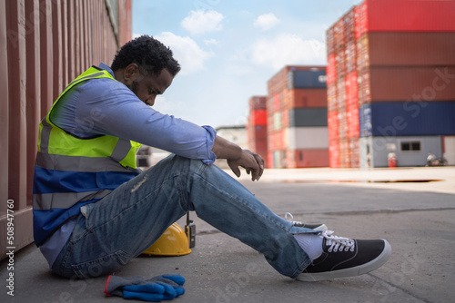 Engineer worker in safety vest sitting and rest in shipping container yard. Feeling tired or unsuccessful on job. Import and export product. Manufacturing transportation and global business concept.