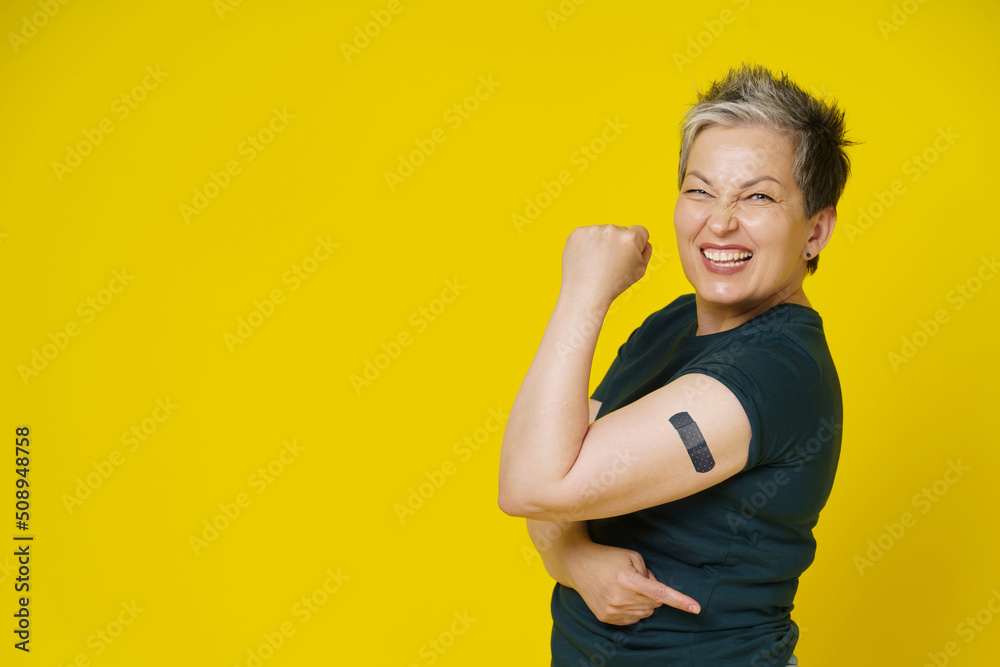 Senior grey haired woman rebelling showing nude shoulder with dark band aid or plaster on it isolated on yellow background. Amazing mature woman 50s. Vaccination and healthcare concept Senior grey haired woman rebelling showing nude shoulder with dark band aid or plaster on it isolated on yellow background. Amazing mature woman 50s. Vaccination and healthcare concept