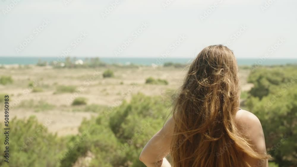 Long hair blows in the wind. Girl is looking at the sea in the distance. Slow mo Long hair blows in the wind. Girl is looking at the sea in the distance. Slow mo
