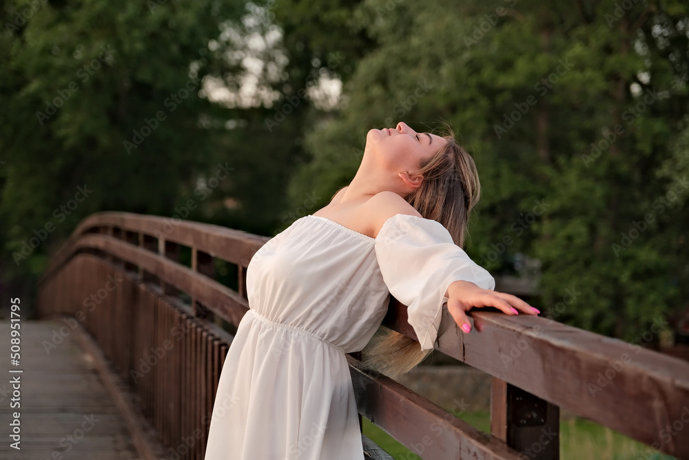 Fototapeta premium a beautiful girl in a white dress stands on a wooden bridge.