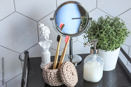 On a white background of a bathtub with a cosmetic bottle, bath accessories, toothbrushes in a glass and houseplants on a background of wall tiles.