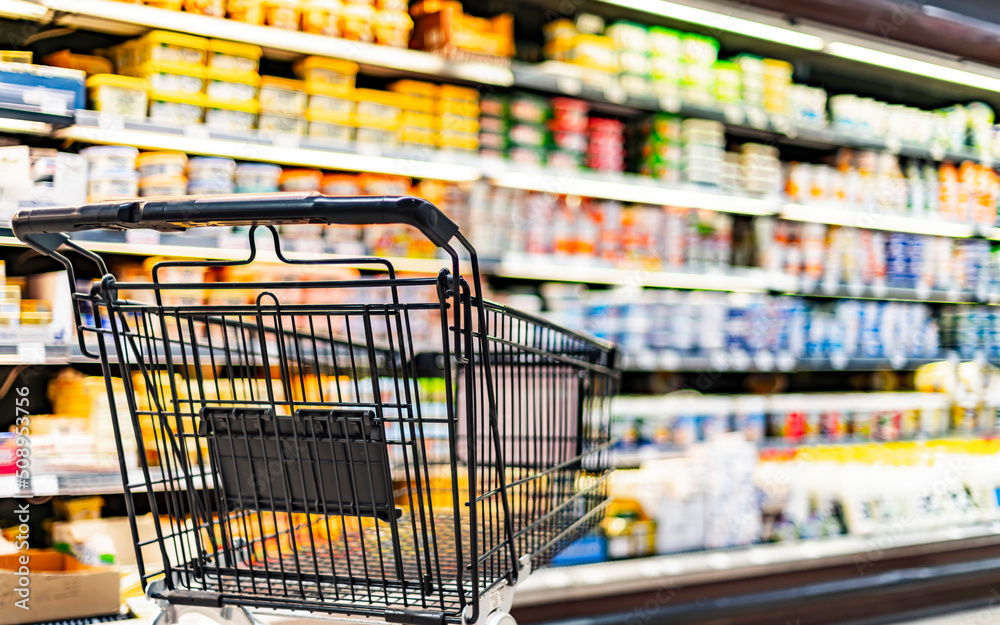 A shopping cart by a store shelf in a supermarket A shopping cart by a store shelf in a supermarket