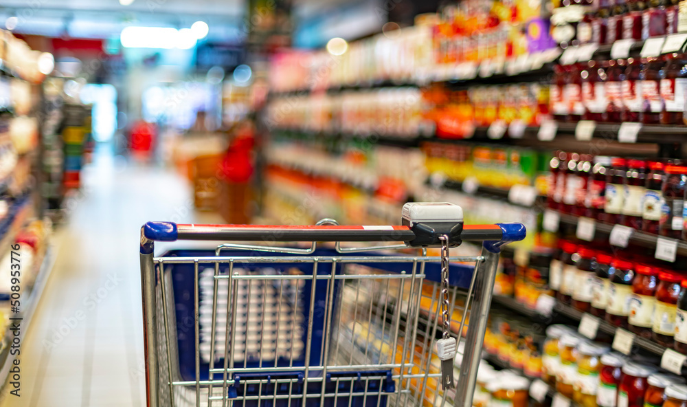 A shopping cart by a store shelf in a supermarket A shopping cart by a store shelf in a supermarket