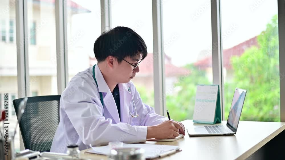 4K Male doctor working with laptop and writing in notebook at table in hospital 4K Male doctor working with laptop and writing in notebook at table in hospital